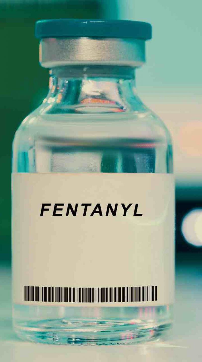 Close-up of a fentanyl vial in a clinical setting with blurred medical bottles in the background